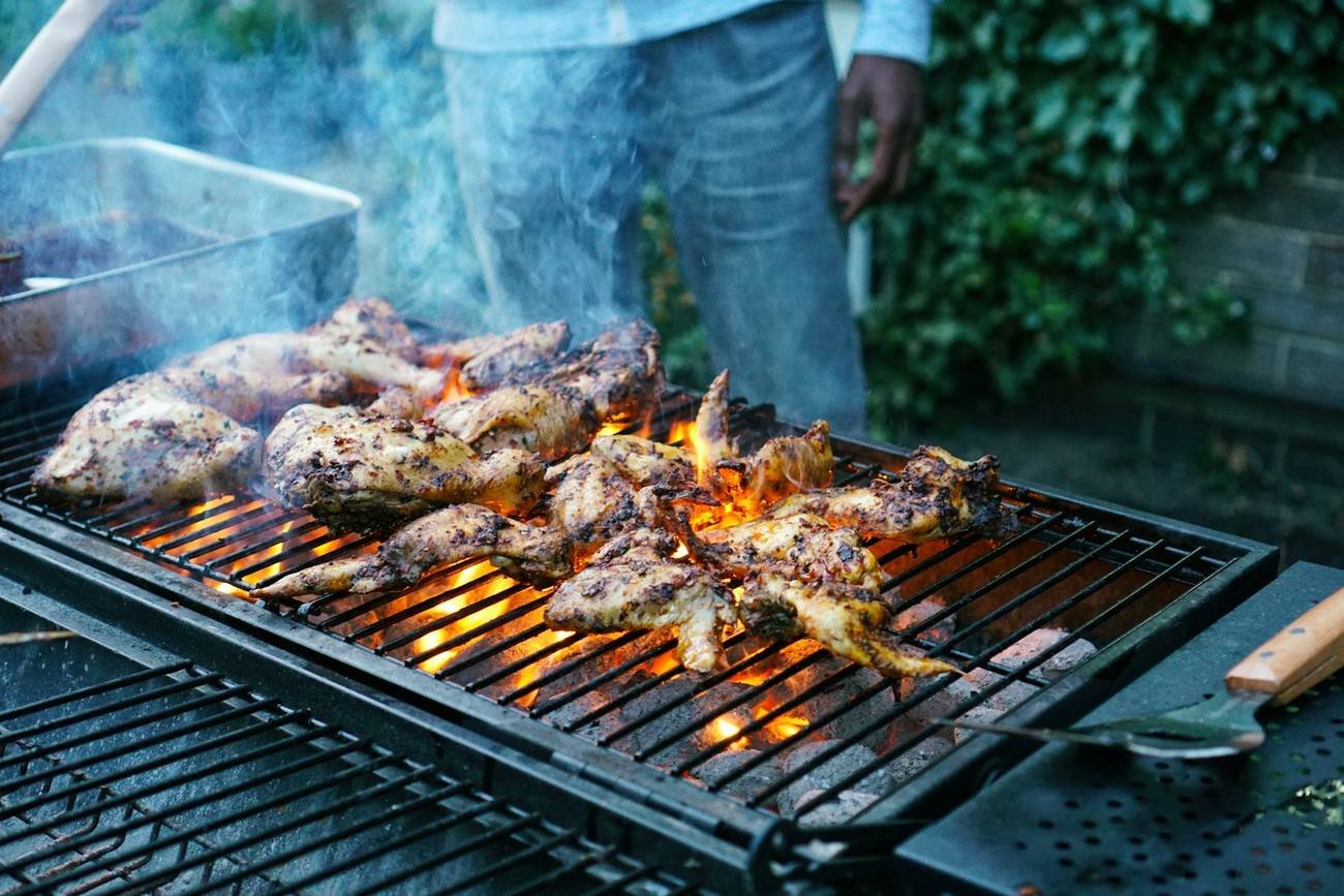 Chicken pieces smoking over a long charcoal grill