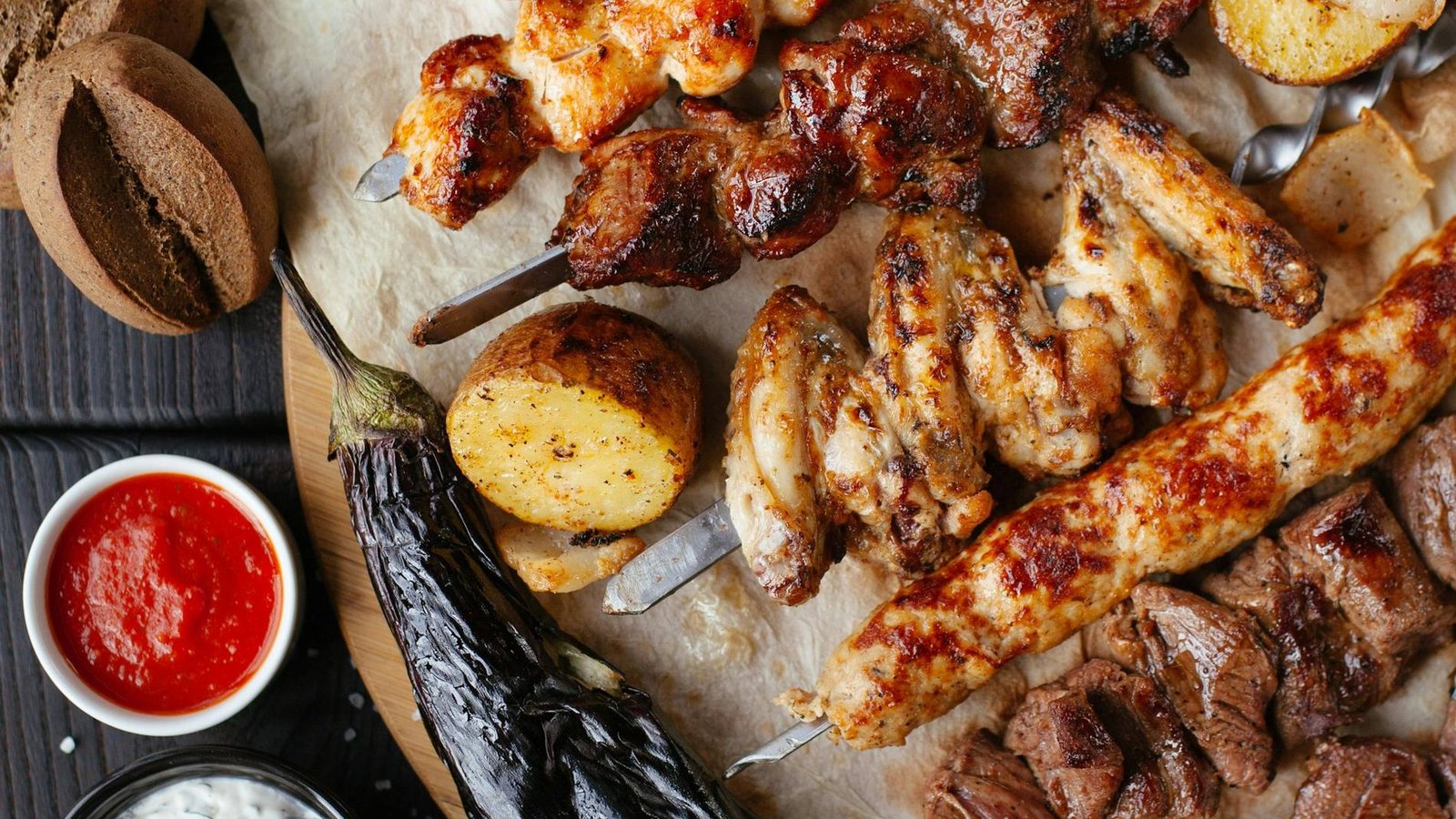 Overhead view of a charcoal mixed grill platter with skewers, kebabs, roast potatoes and chutneys
