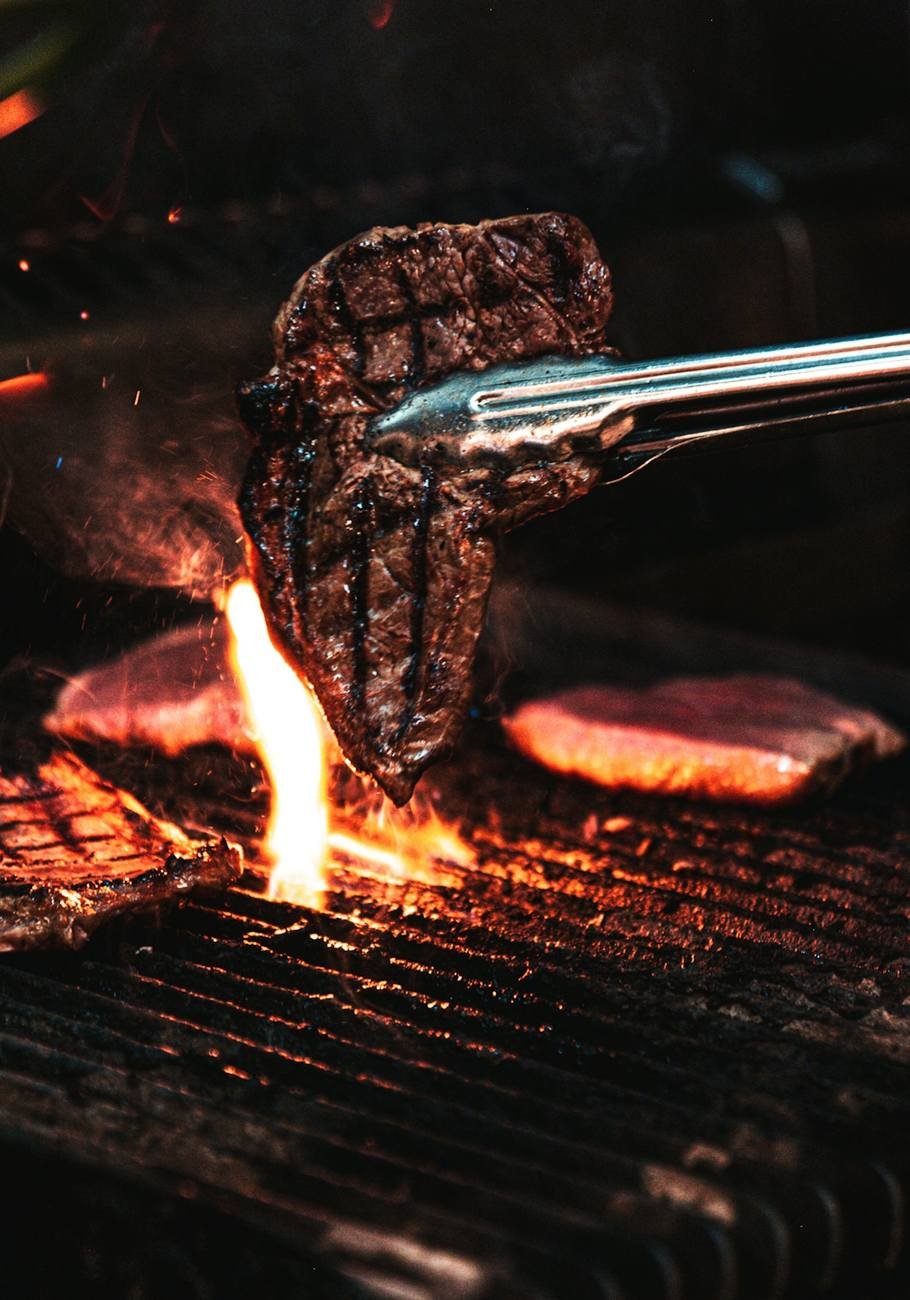 Tongs lifting a seared steak above an open flame
