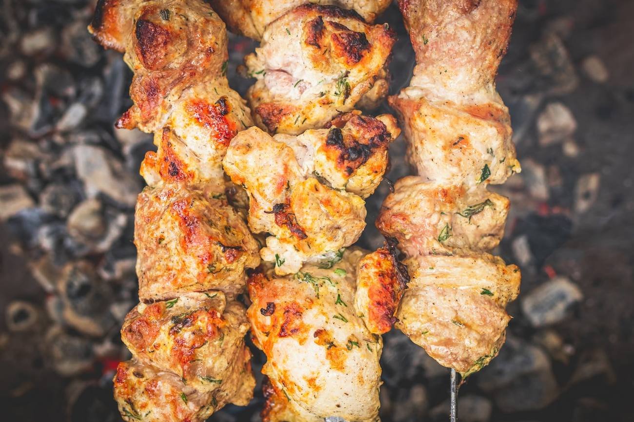 Chicken tikka skewers turning over glowing charcoal