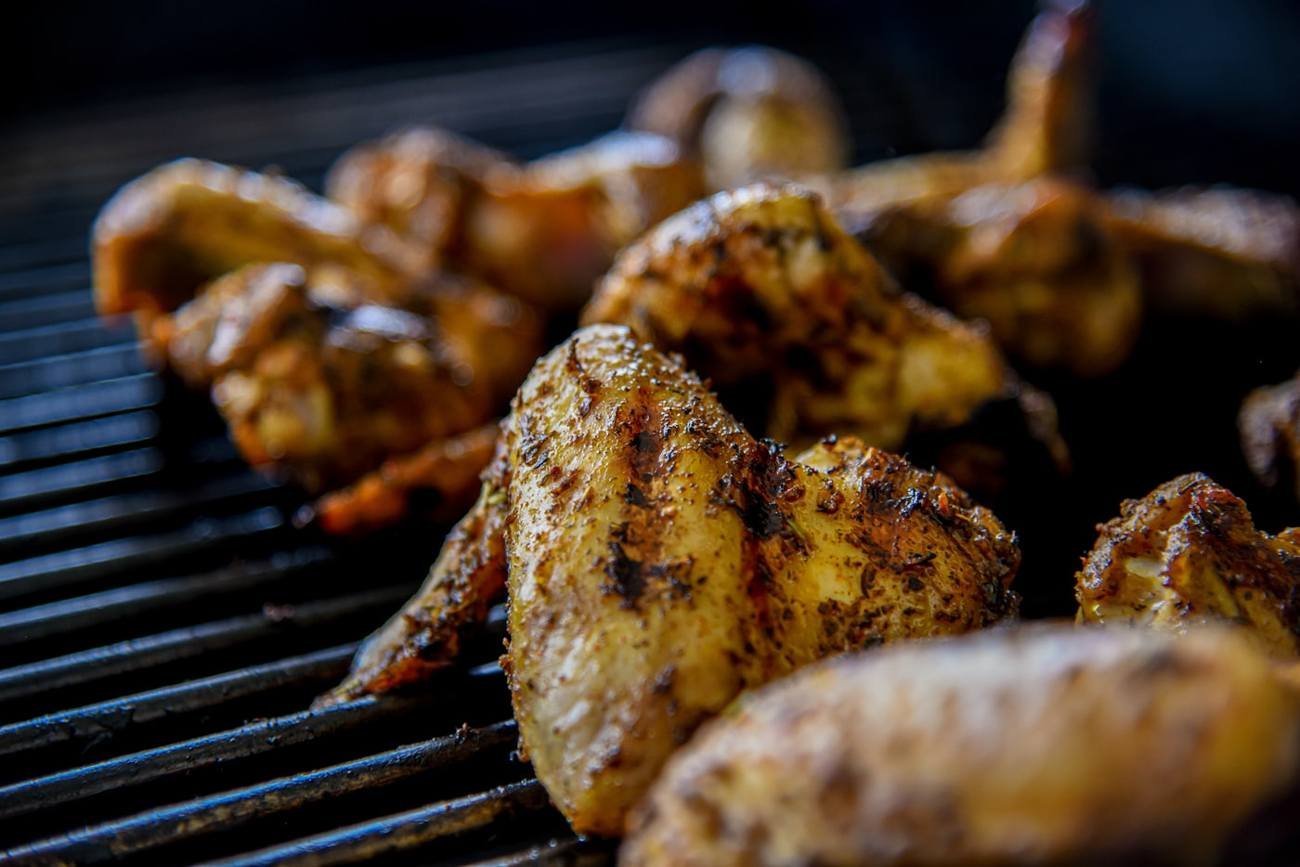 Spiced chicken wings and drumsticks browning on the grill bars